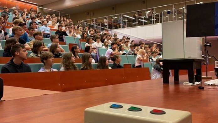 aula na której są uczestnicy spotkania, oraz na ladzie wykładowej jest urządzenie